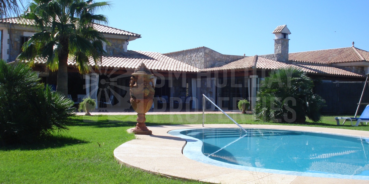 Fachada de la villa desde la piscina y parking exterior privado para estacionar varios vehículos.